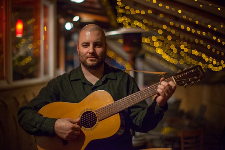 A man holding a guitar in front of lights.