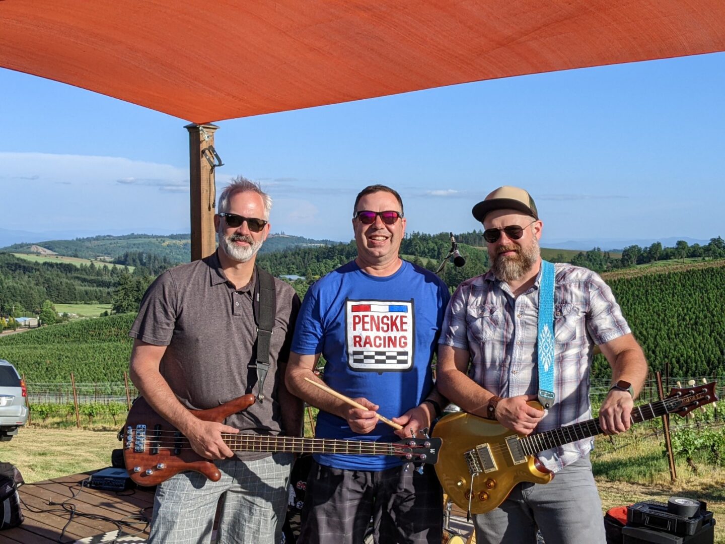Three men standing under a tent with guitars.