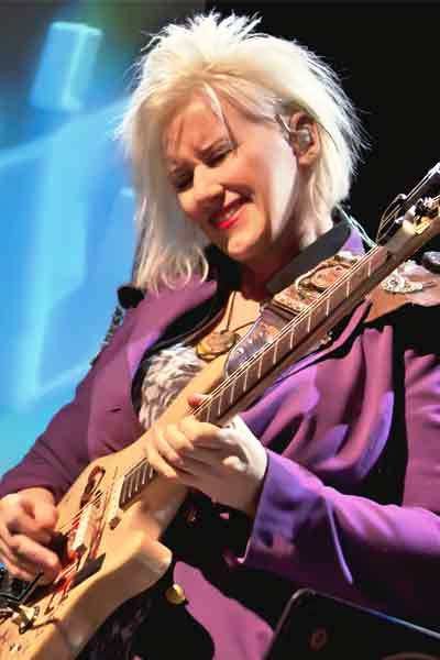A woman in purple jacket playing an electric guitar.