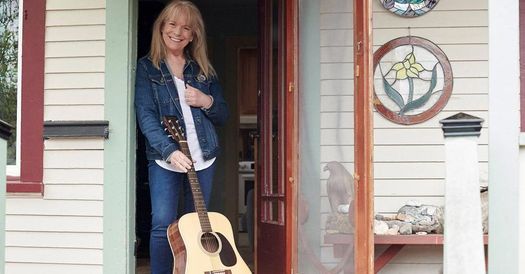 A woman standing in front of a door with a guitar.